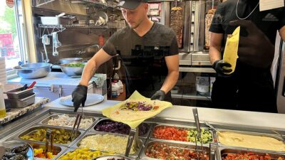 The owner of Shawarma Paradise filling a laffa with hummos, tehini, and salad