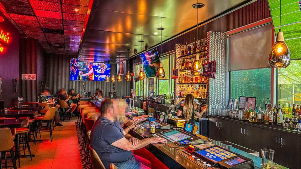 Gaming lounge and bar inside Carmine's Pizza Kitchen with illuminated machines, televisions, and liquor shelves