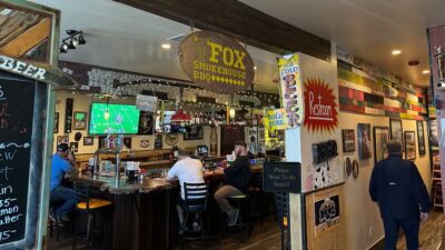 Bar area at Fox Smokehouse BBQ with open seating, TV screens, and full bar.