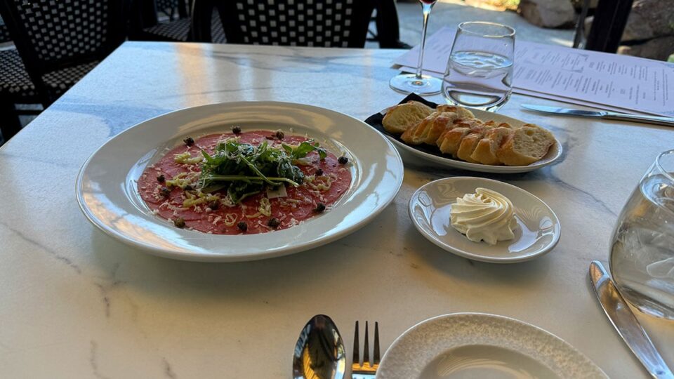 Plate of Beef Carpaccio at Marché Bacchus, topped with arugula, shaved parmesan, and capers.