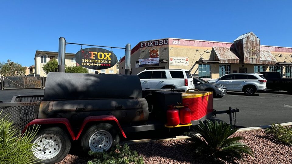 Working smoker outside Fox Smokehouse BBQ with restaurant in the background.