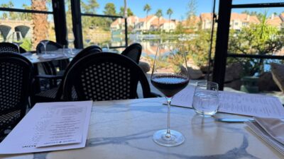A glass of red Pinot Noir on a patio table at Marché Bacchus with the calm waters of Lake Jacqueline behind it.