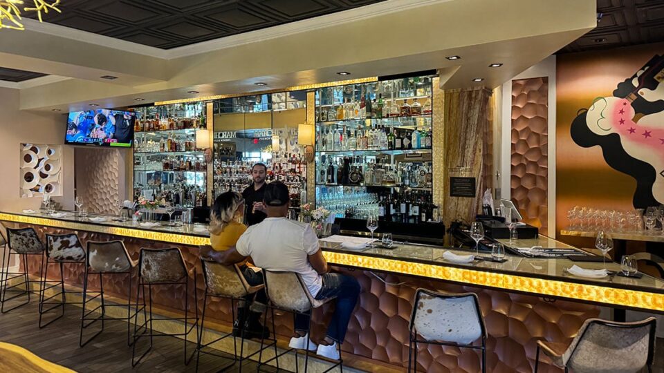 Bartender pouring drinks behind the full bar at Marché Bacchus while a couple enjoys their cocktails.