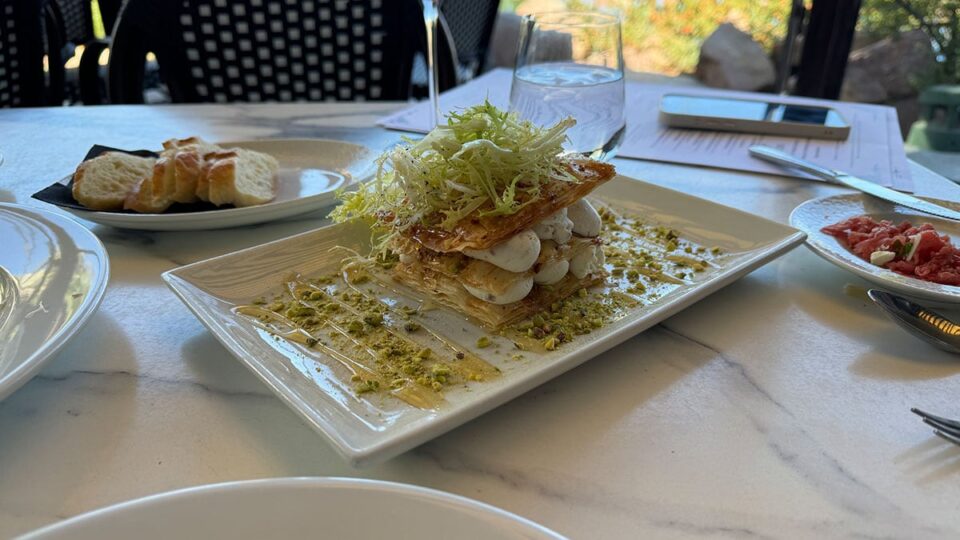 Close-up of the Truffled Goat Cheese Napoleon at Marché Bacchus, showing phyllo layers, pistachios, and honey drizzle.