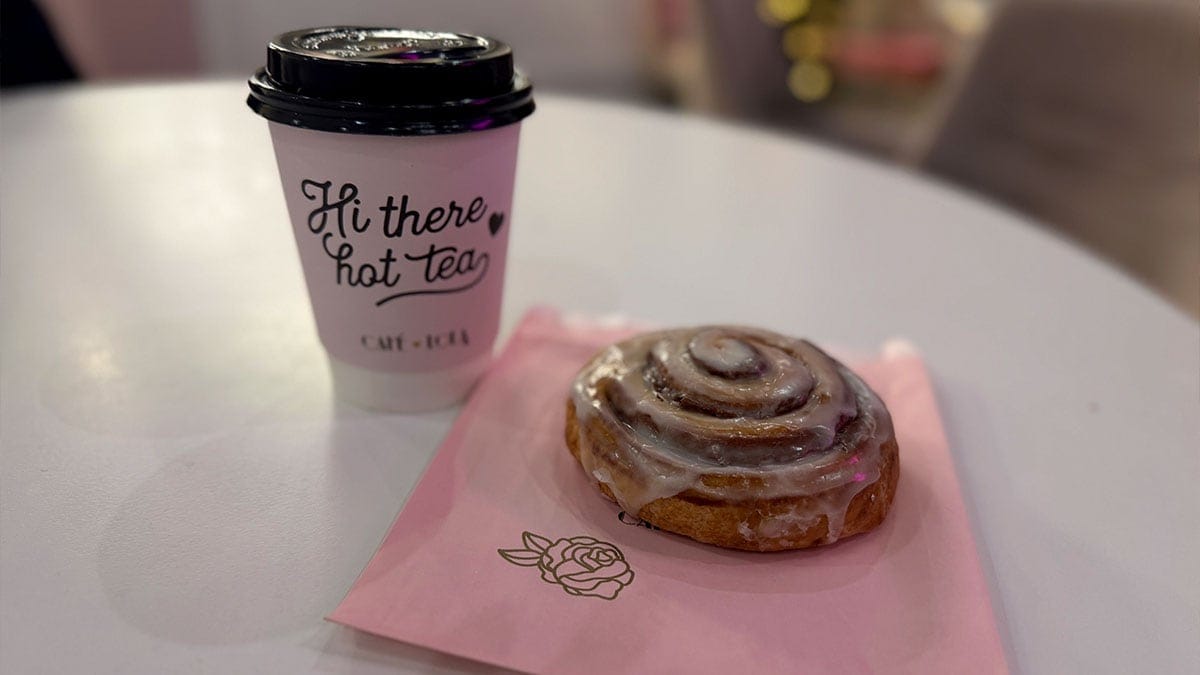 Latte in a cup next to a cinnamon roll topped with icing, displayed on a café table for a warm and inviting treat.