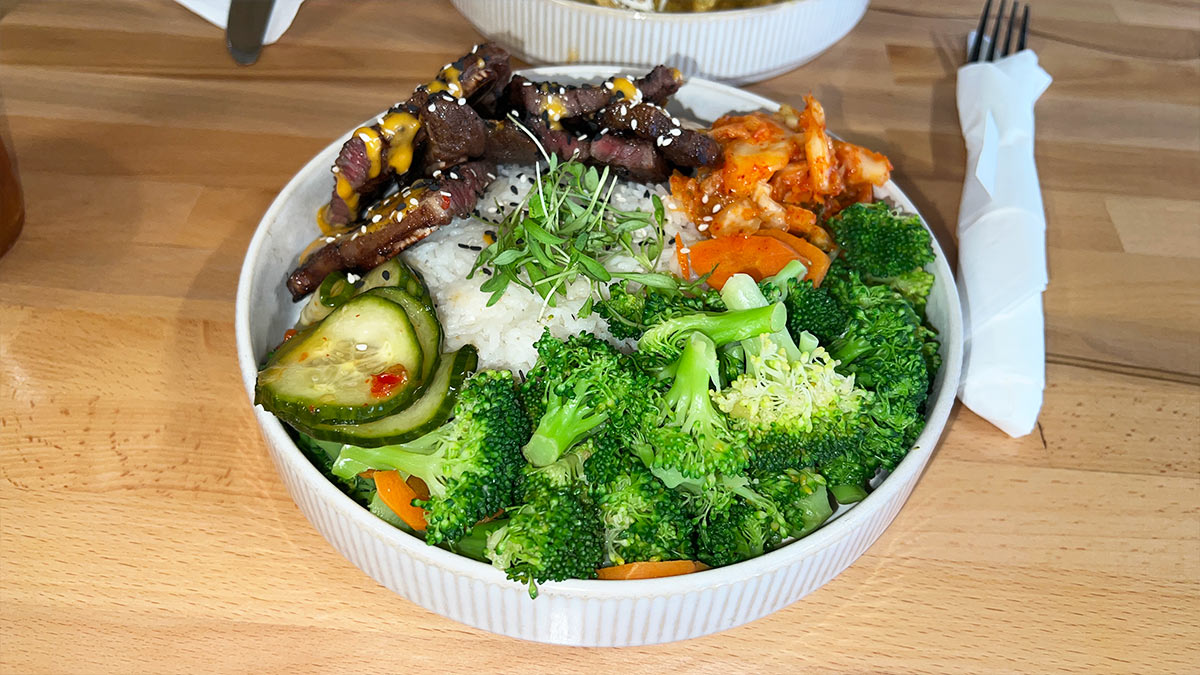 Korean Beef Bowl with marinated short rib, jasmine rice, broccoli, cucumbers, kimchi, and sesame seeds in a white bowl.