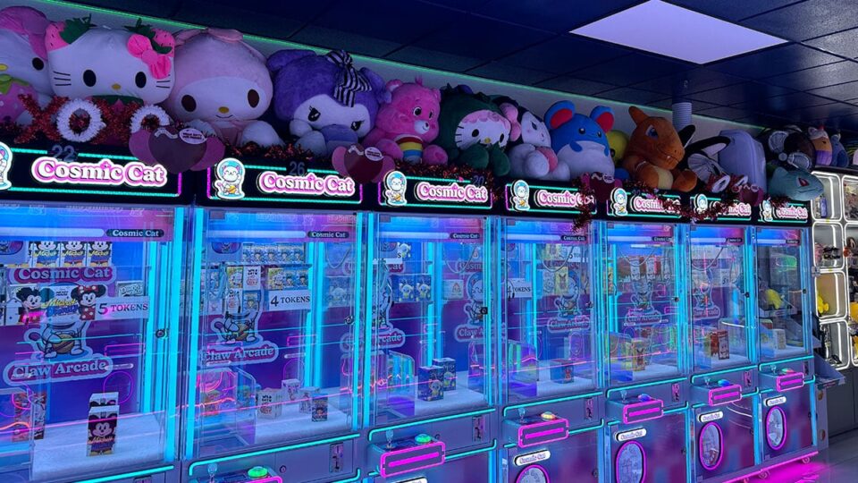 Row of claw machines with giant plushies on top at Cosmic Cat Claw Arcade in Las Vegas.