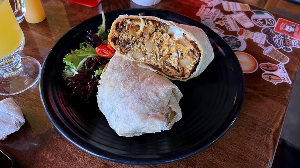 Breakfast burrito cut in half on a black plate with mixed greens and a cherry tomato.