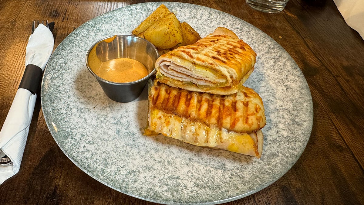 Medianoche Cuban sandwich with ham, turkey, pickles, provolone, and chipotle mayo on pressed Cuban bread, served with potato hash.