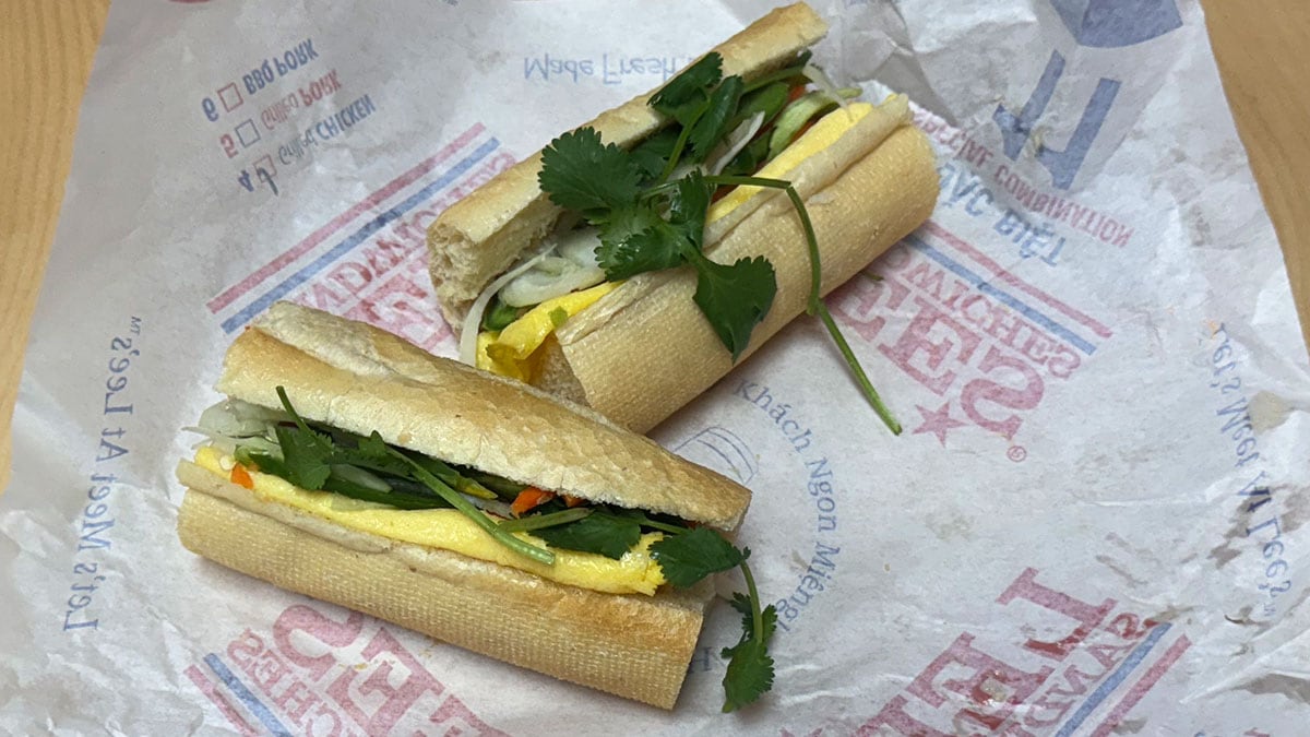 Egg banh mi sandwich on a toasted baguette with cooked eggs, pickled carrots and daikon, fresh cucumber, cilantro, and sauce.