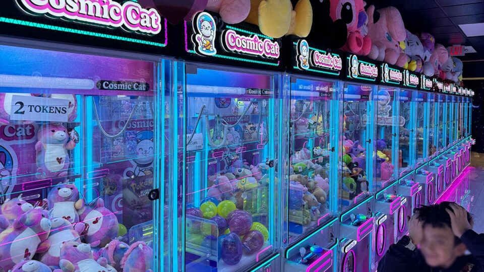 Child trying to grab a plushie inside a claw machine at Cosmic Cat Claw Arcade.