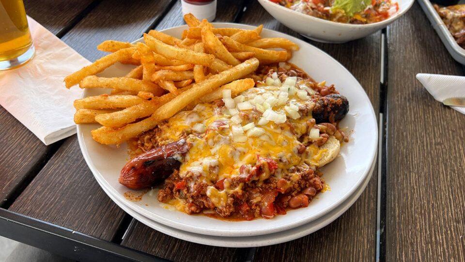 Chili dog topped with sauce and served with crispy fries at Big T’s Cantina