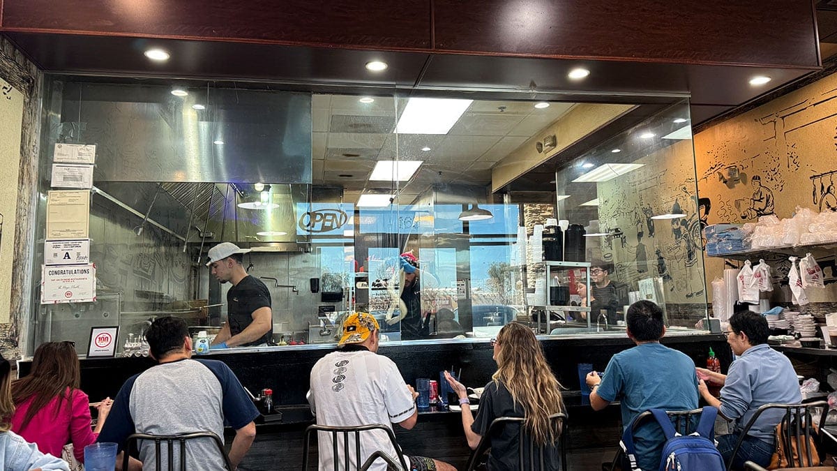 chefs hand-pulling fresh noodles behind a glass window at The Magic Noodle Las Vegas.