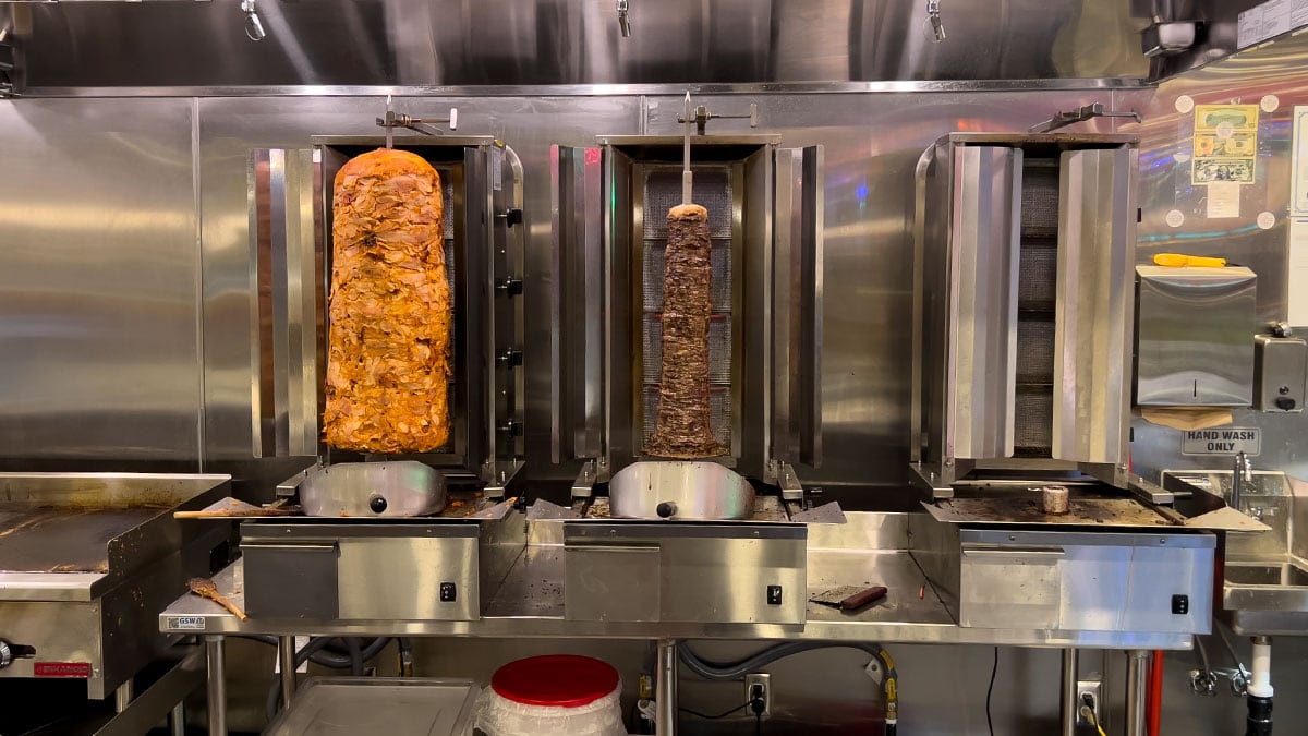 shawarma meat stacked on a vertical rotisserie stand cooking and slowly roasting in a restaurant kitchen