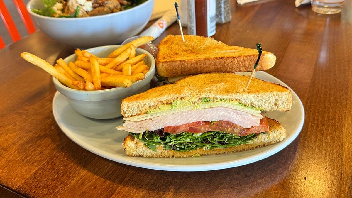 Smoked turkey and avocado sandwich with Swiss cheese, greens, tomatoes, and chipotle mayo served with fries at Rachel’s Kitchen