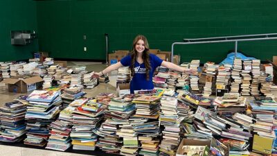 Sophia Booth standing with stacks of collected donated books