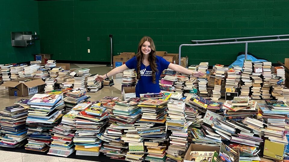 Sophia Booth standing with stacks of collected donated books
