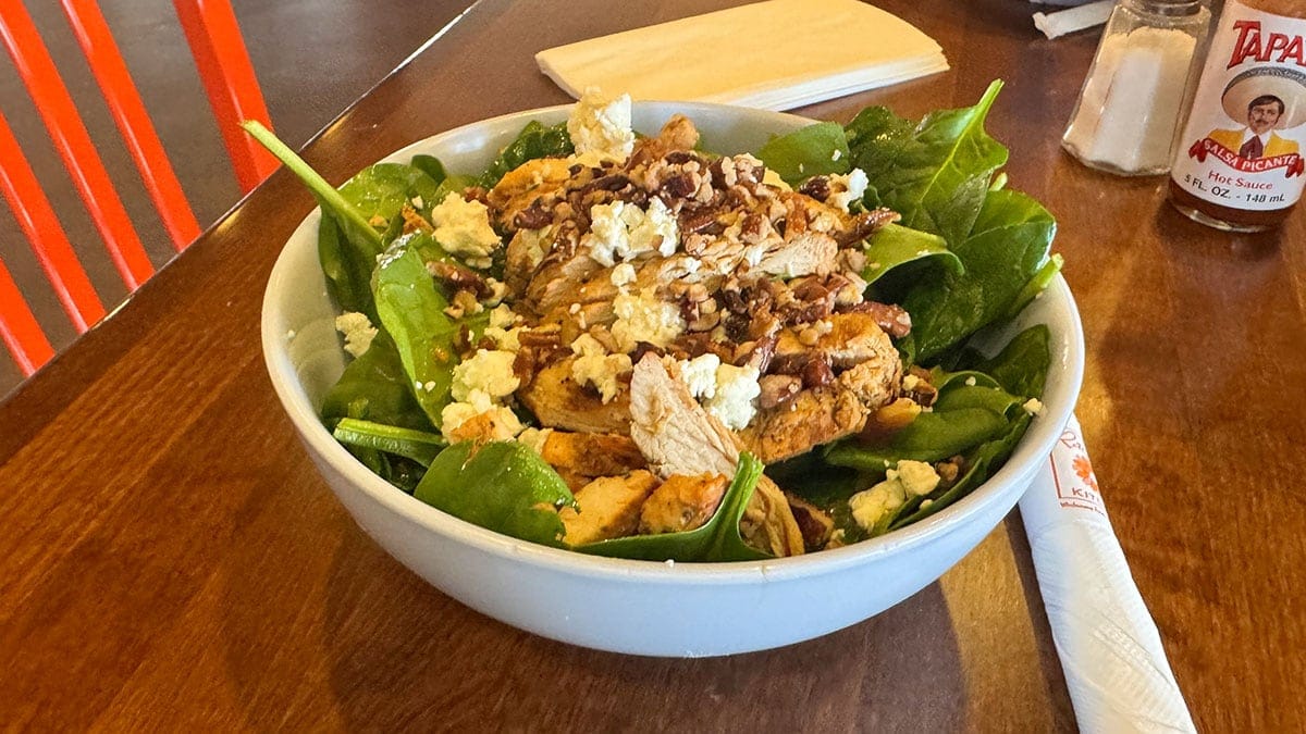 Spinach salad from Rachel’s Kitchen featuring baby spinach, bacon, tomatoes, mushrooms, caramelized pecans, and goat cheese