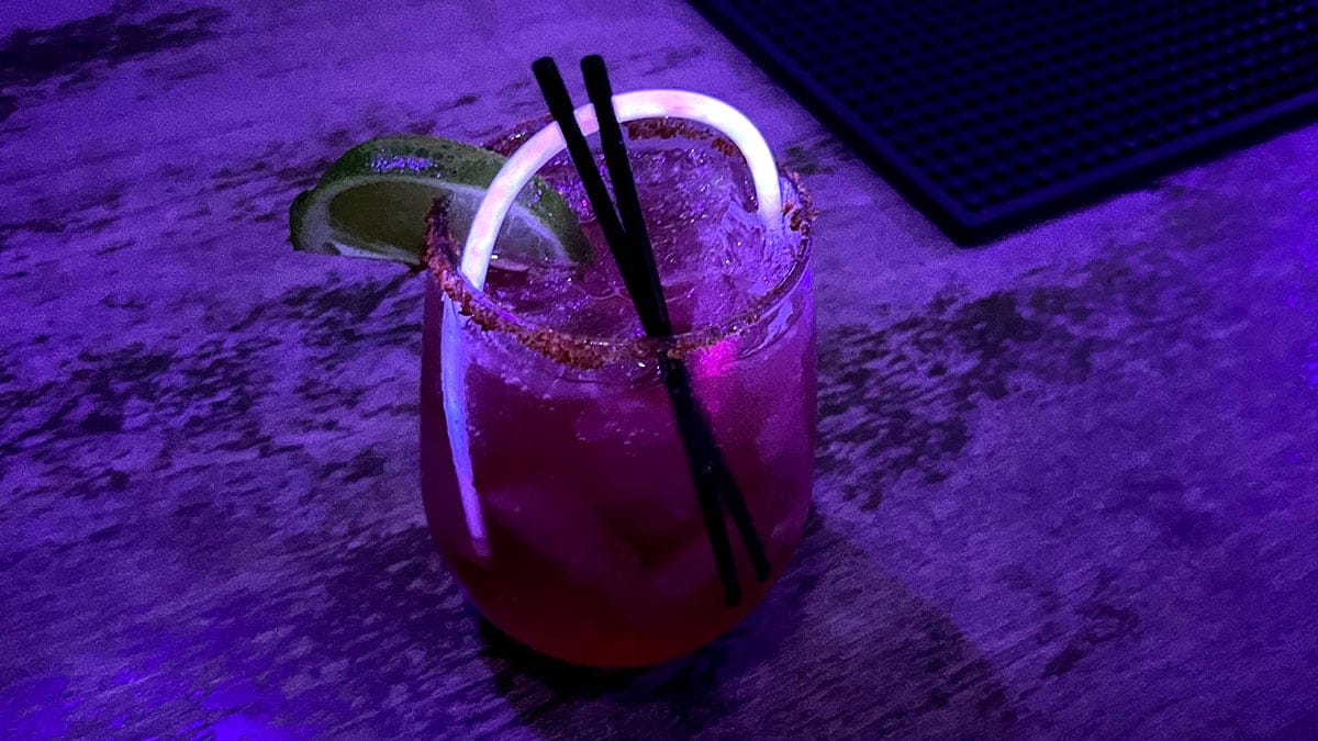 Watermelon-tequila cocktail with a Tajín rim and glow stick garnish at Raised By Wolves inside Neonopolis.