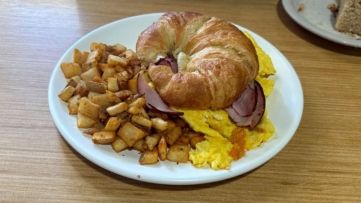 croissant breakfast sandwich with eggs ham cheese and fries at The Cracked Egg