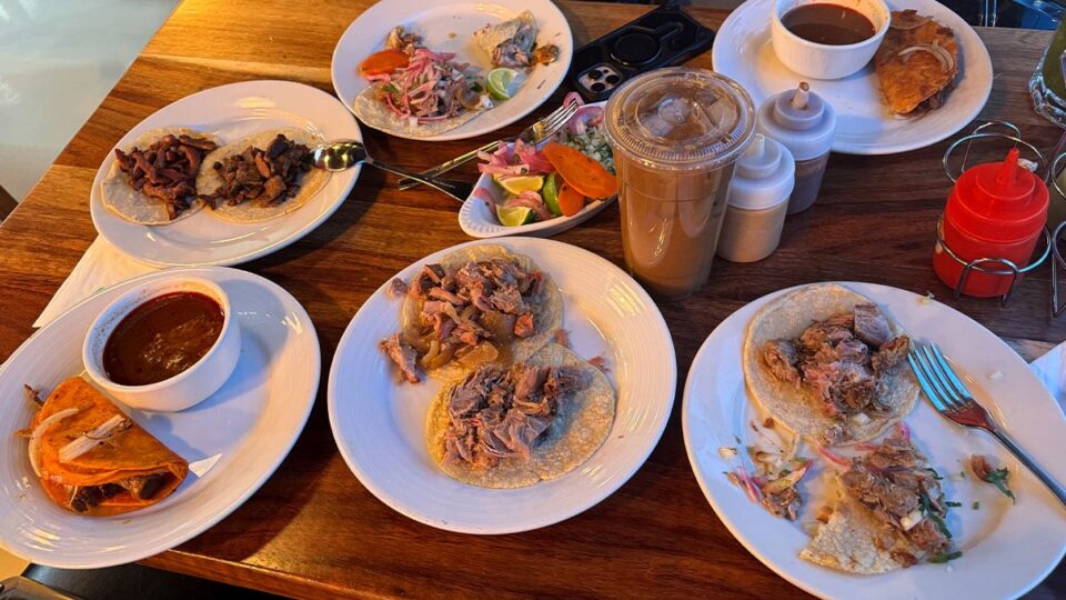 Full table spread of tacos including birria, carnitas, and al pastor at Carnitas y Tortas