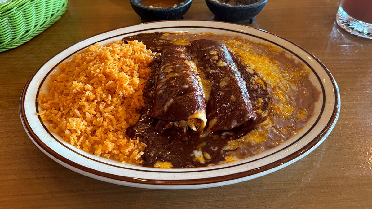 chicken mole enchiladas topped with rich mole sauce and served with rice and beans