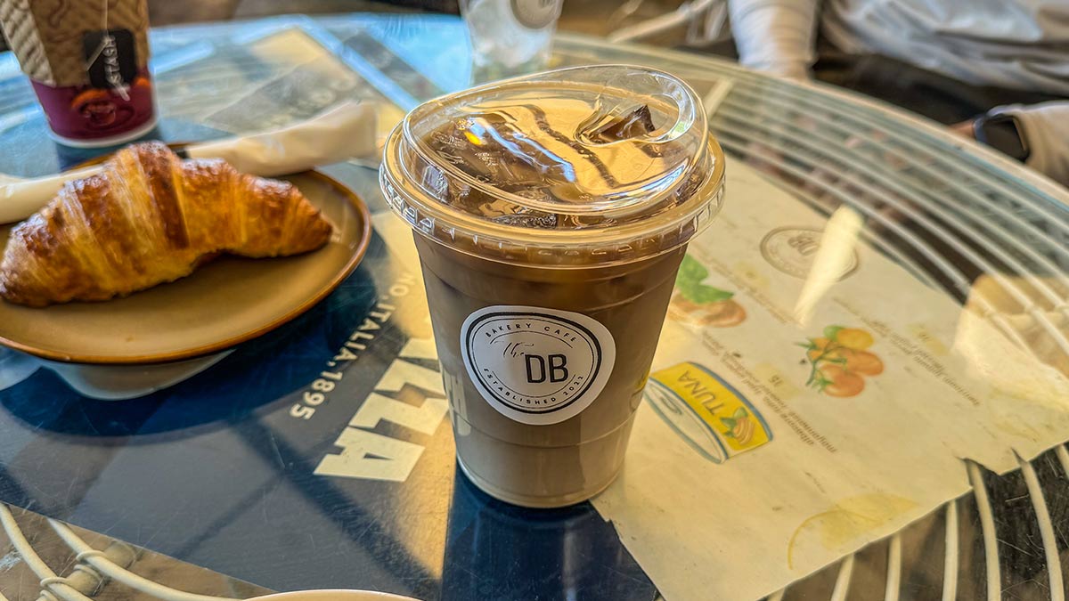 Cold brew coffee in a plastic cup on a patio table next to a croissant.