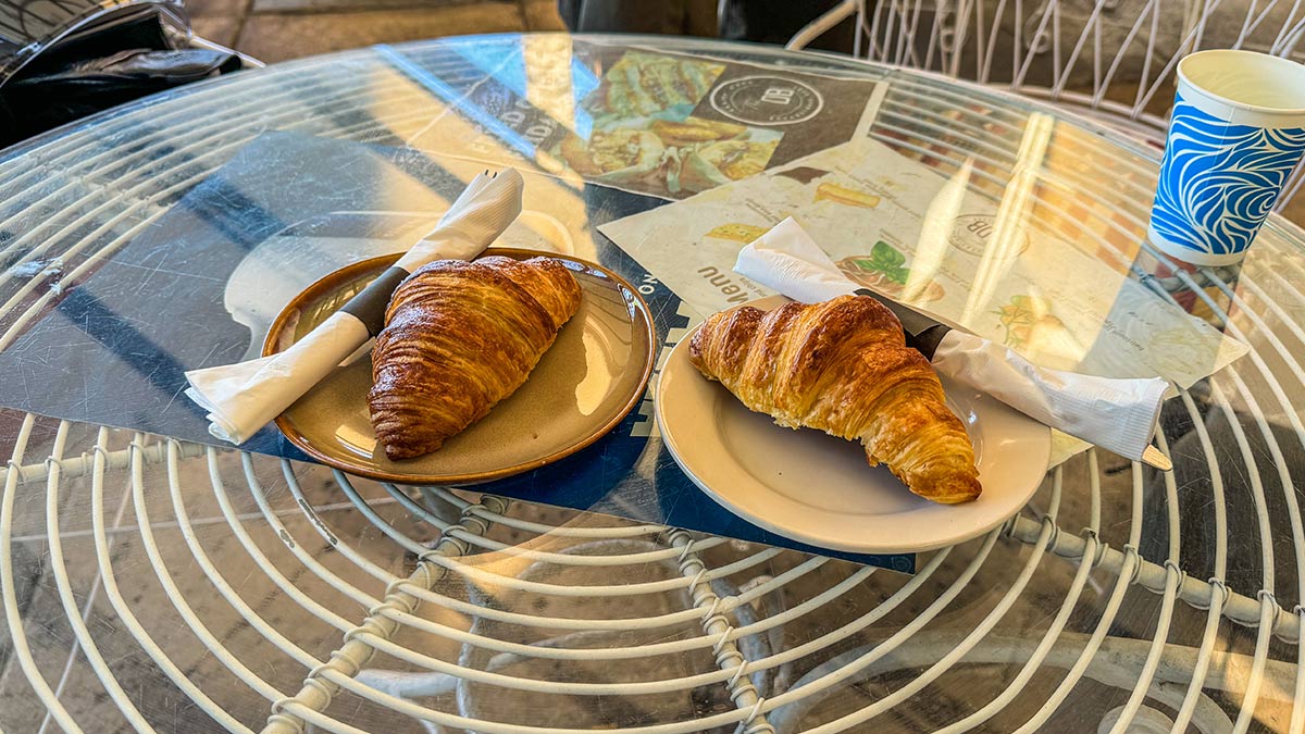 Two butter croissants served on plates at an outdoor patio table.