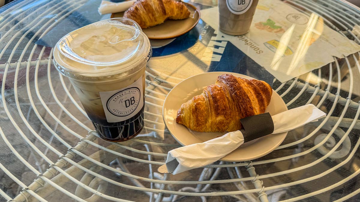 Iced coffee and croissant served on a glass patio table.