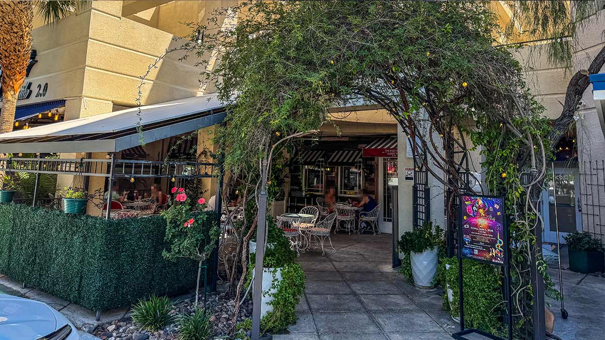 Outdoor patio entrance with greenery and seating outside a bakery cafe.