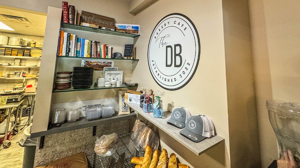 Interior wall with The Daily Bread Bakery Cafe logo, bread shelves, hats, and visible bakery kitchen area.