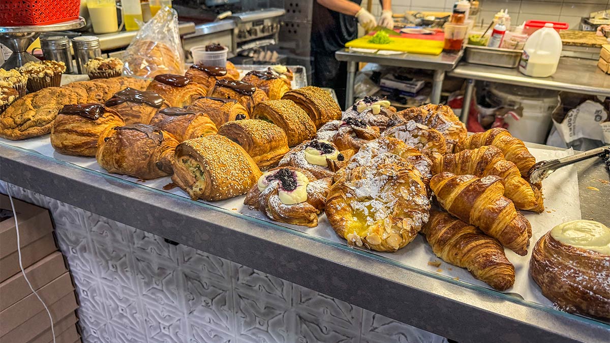 Pastry display filled with croissants, danishes, cookies, and baked goods at a bakery counter.