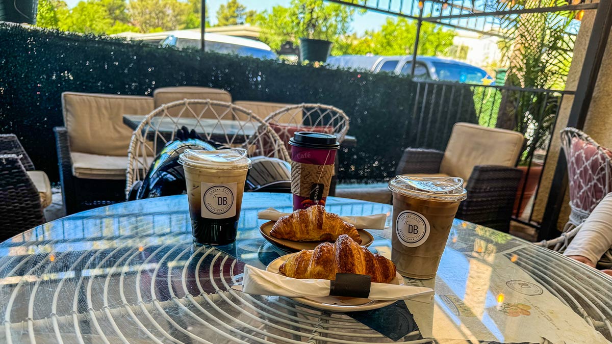 Patio table with croissants, iced coffee drinks, and outdoor seating area.