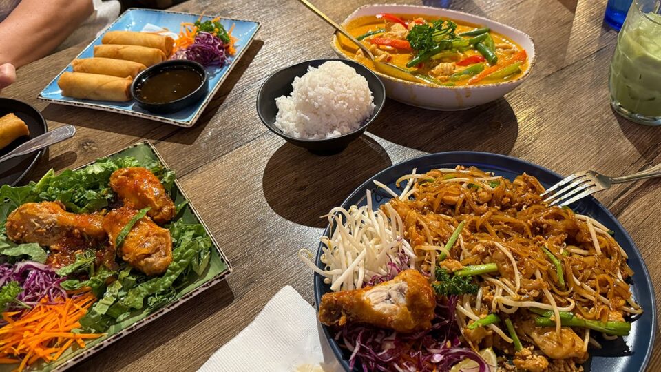 Thai food spread with Pad Thai, Panang curry, spring rolls, wings, and Thai green tea at Sen Thai Noodles