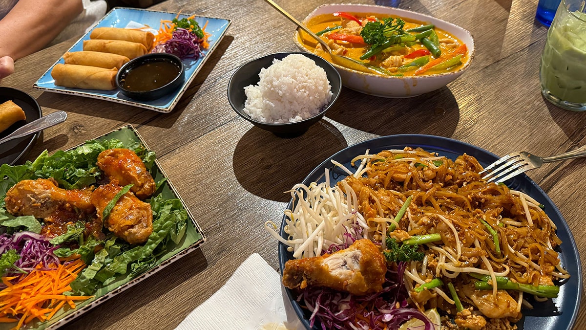 Thai food spread with Pad Thai, Panang curry, spring rolls, wings, and Thai green tea at Sen Thai Noodles