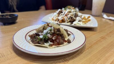 Carne asada tacos served with loaded fries topped with cheese, meat, and fresh garnishes at Sin Fronteras Tacos y Más.