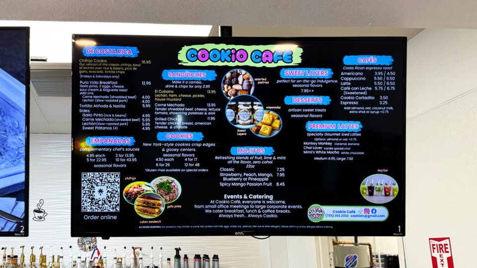 Digital menu board displaying drinks, desserts, sandwiches, cookies, and empanadas at Cookio Cafe.