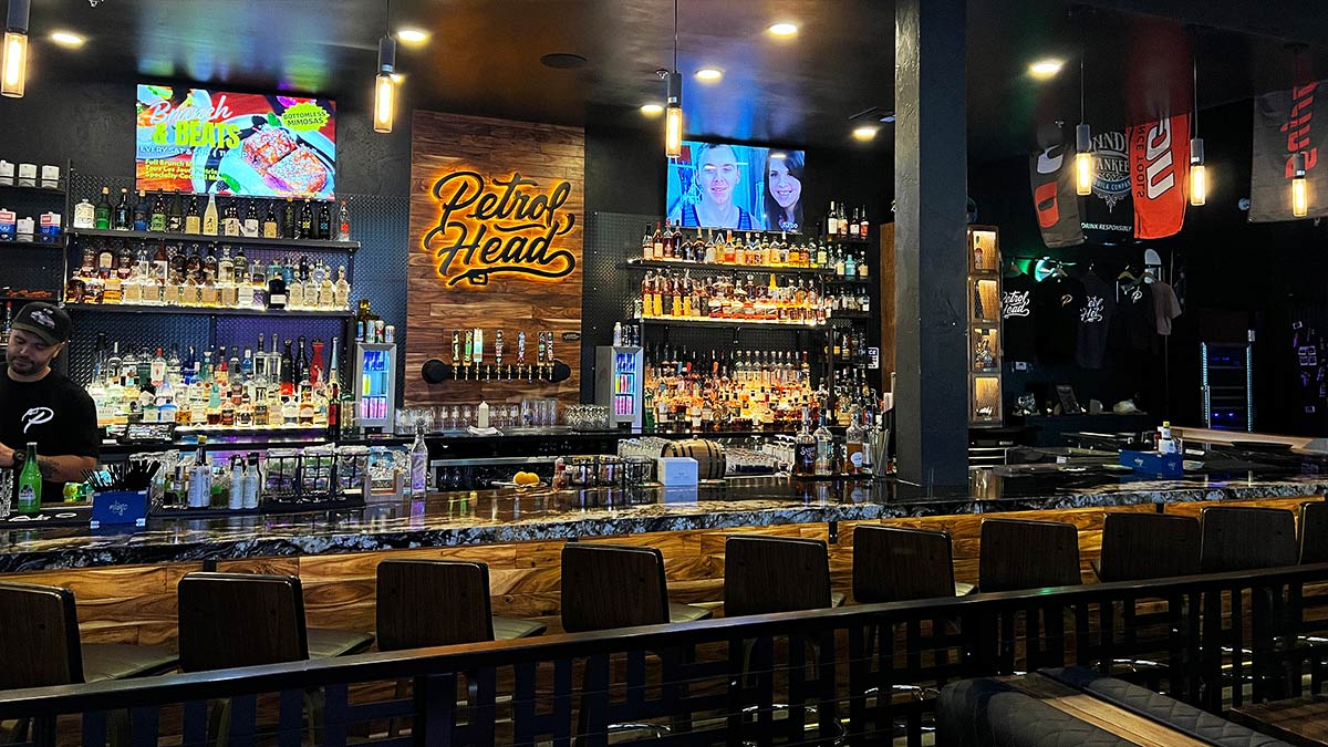 Fully stocked main bar with illuminated Petrol Head logo, beer taps, bottles, and televisions.