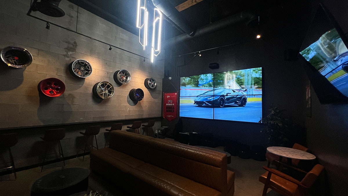 Private lounge with mounted wheels, couches, and large video wall at Petrol Head Bar & Grill.