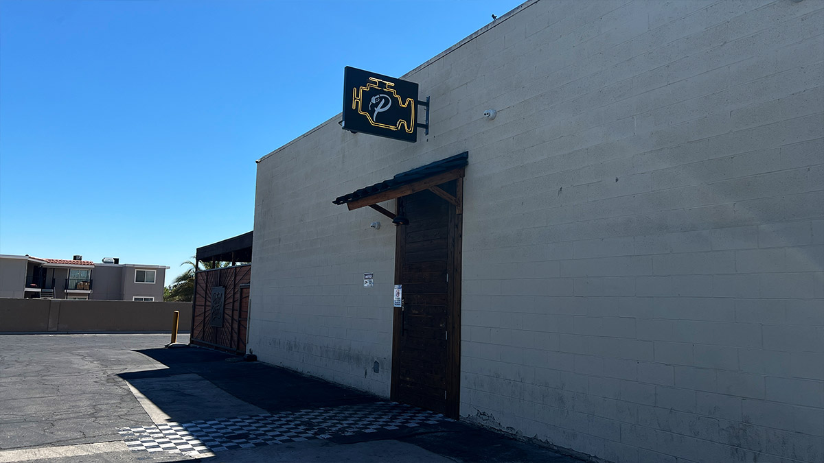 Rear entrance to Petrol Head Bar & Grill in Las Vegas with engine-shaped sign and large parking lot.
