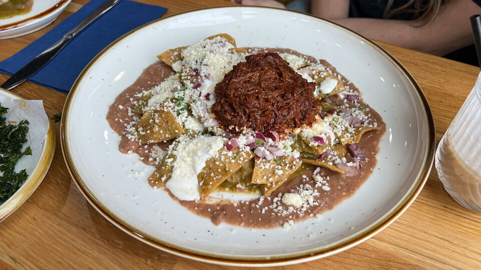 Chilaquiles with beef barbacoa, green tomatillo salsa, refried beans, sour cream, and onion