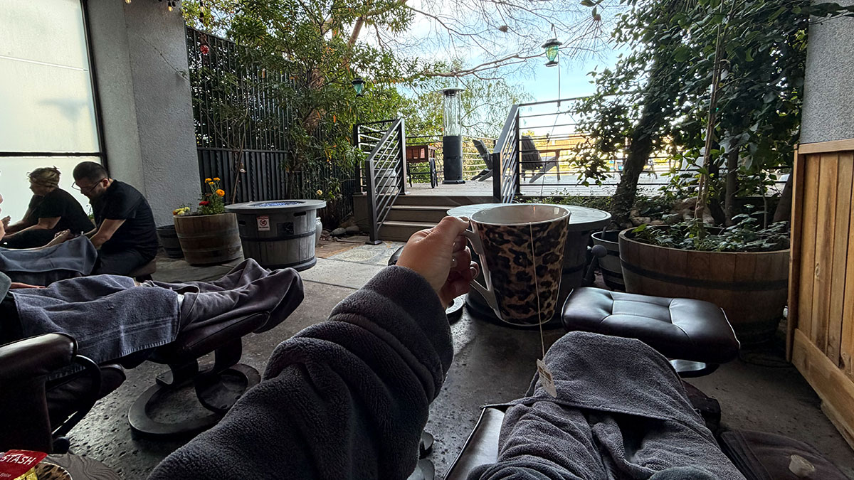 Guest holding a cup of hot tea while relaxing in a recliner on the outdoor patio at The Spa at Lakeside.