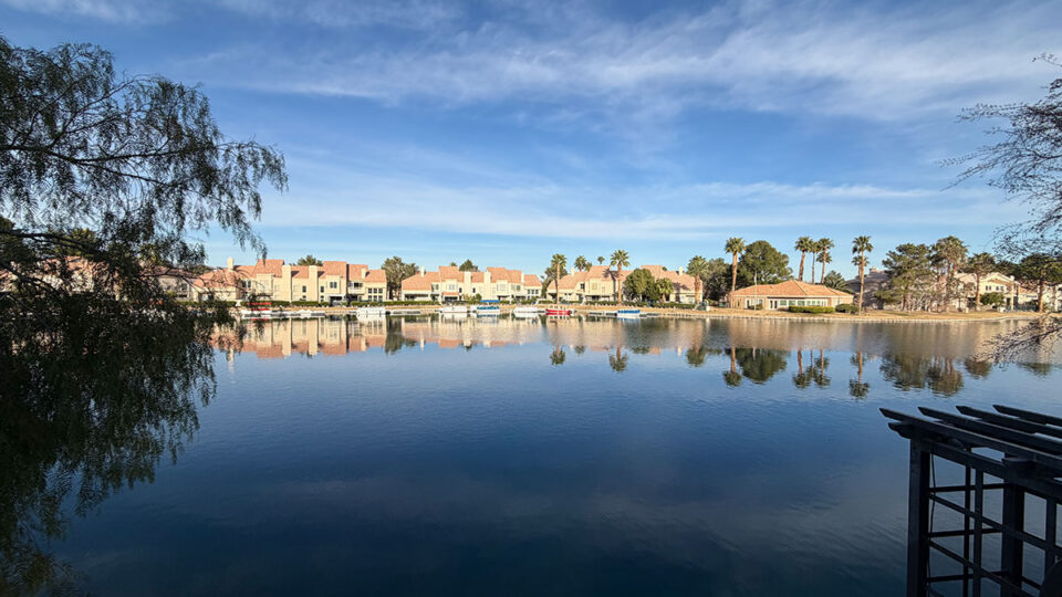 Calm waters of Lake Jacqueline reflecting waterfront homes and palm trees in the Desert Shores neighborhood of Las Vegas.