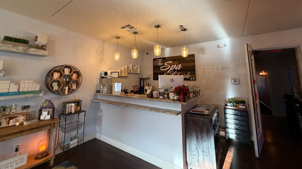 Reception desk with pendant lighting, skincare displays, and The Spa at Lakeside 2.0 wall sign.