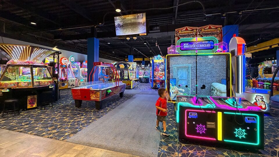 Air hockey table and illuminated Marksman shooting arcade game at Round1, surrounded by colorful video game machines.