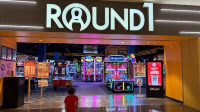Large illuminated Round1 sign above the entrance to the arcade, with colorful video games visible inside.