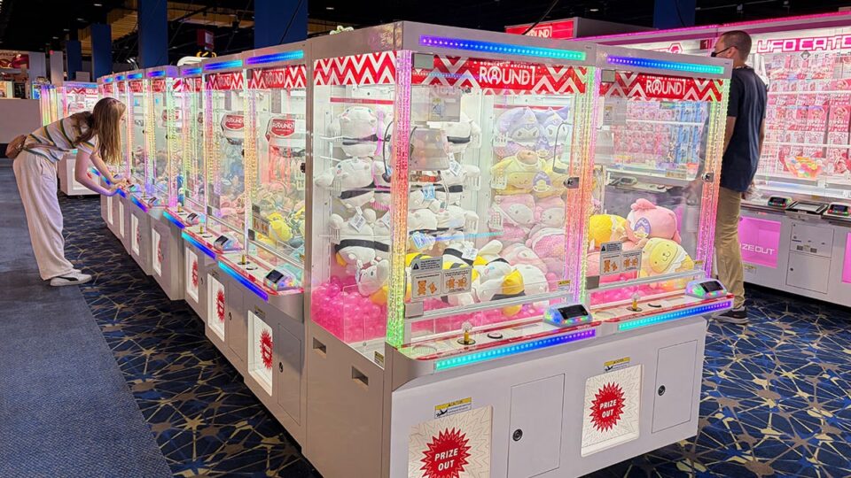 Long row of brightly lit claw machines filled with plush prizes as visitors play games inside Round1 Bowling & Arcade.